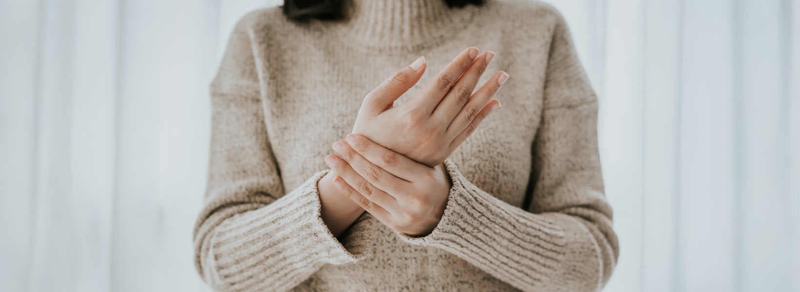 Henkilö kuvattuna kaulasta vyötäröön. Henkilö pitää toisella kädellä toisen käden ranteesta kiinni.